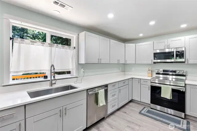 New appliances and vinyl plank flooring in the kitchen with drop in stainless sink.