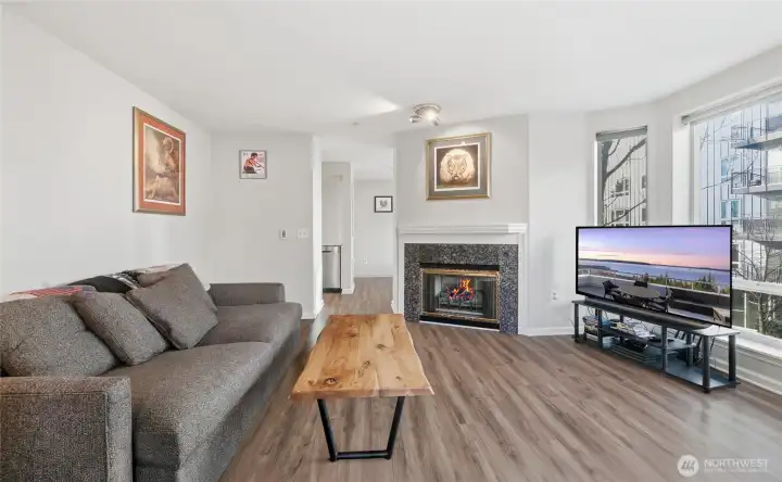 Living room with gas fireplace and floor to ceiling windows. Windows have remote control blinds. Updated LVP flooring.