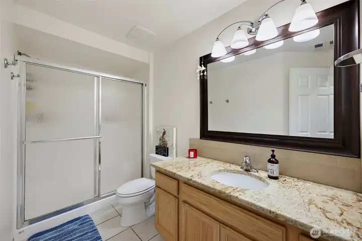 Lower level 3/4 bathroom with granite countertop, ceramic tile & plenty of lighting.