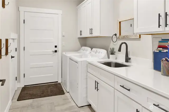 This spacious utility room includes the laundry facilities, a deep utility sink, storage room, generous cabinetry and access to the garage, which is deep and oversized.