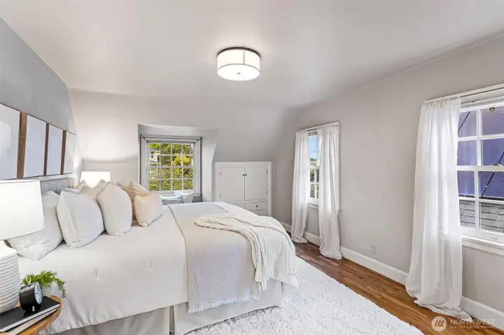 This dreamy primary bedroom spans the length of the house and features windows on 3 sides overlooking the landscaped grounds. The hardwood floors are recently refinished.