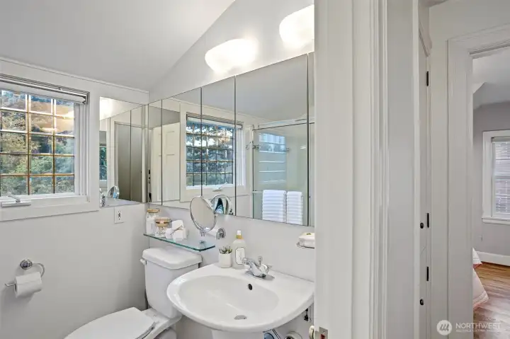 The upstairs full bathroom has marble tile flooring, a tub with tempered glass doors, a new toilet and a beveled glass double-pane window overlooking the gardens.