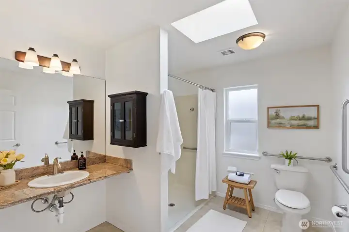 Bathroom off the primary has ADA features like a roll in shower with a wall mounted seat and grab bars.