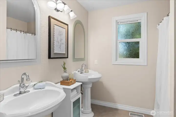 Main floor bathroom with double pedestal sinks, ceramic tile floors and walk-in shower.