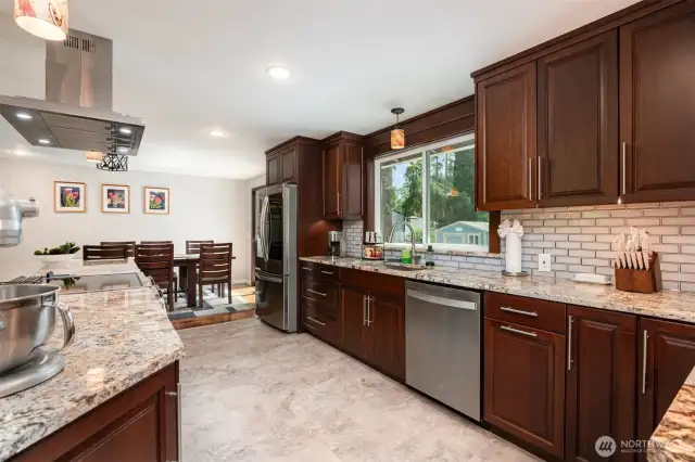 Another angle showcasing all the counter space with granite counters and additional deep wood cabinets.