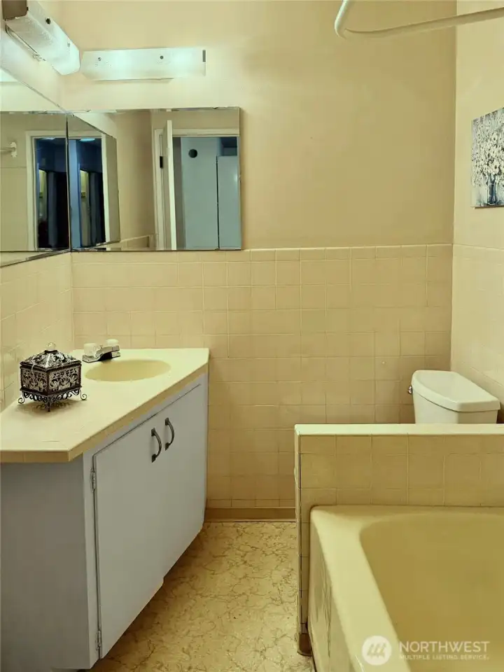 The full bathroom with the original yellow tile and tub.