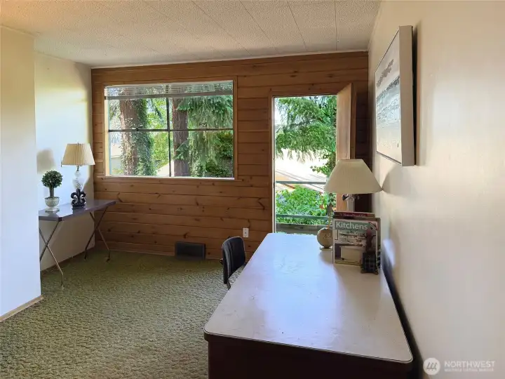 Another bedroom on the main floor with access to the back deck. Under the carpet is a plywood floor. The original knotty pine wall remains. How would you redecorate this room?