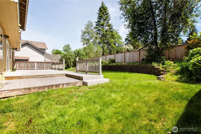 Spacious back yard with retaining wall and fence.