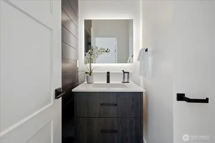 The powder room has a shiplap accent wall, a floating cabinet, and a backlit mirror.