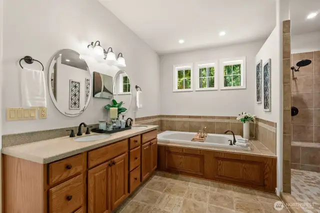 The primary bathroom offers a spacious retreat, featuring dual vanities set on an expansive countertop, a luxurious soaking tub, and a large walk-in shower complete with a built-in bench and tiled wall shelf. Redesign the space to create your own personal spa space.
