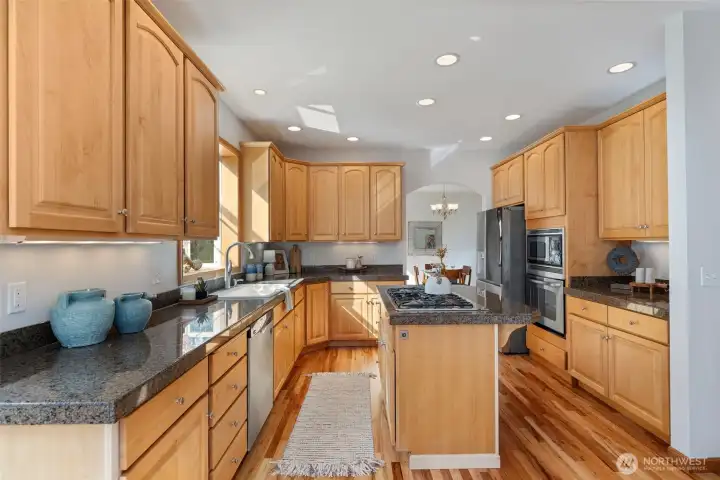 The kitchen boasts a center island with a gas stovetop & electric recessed over fan, tall classic wood cabinetry offering ample storage, and elegant granite countertops.