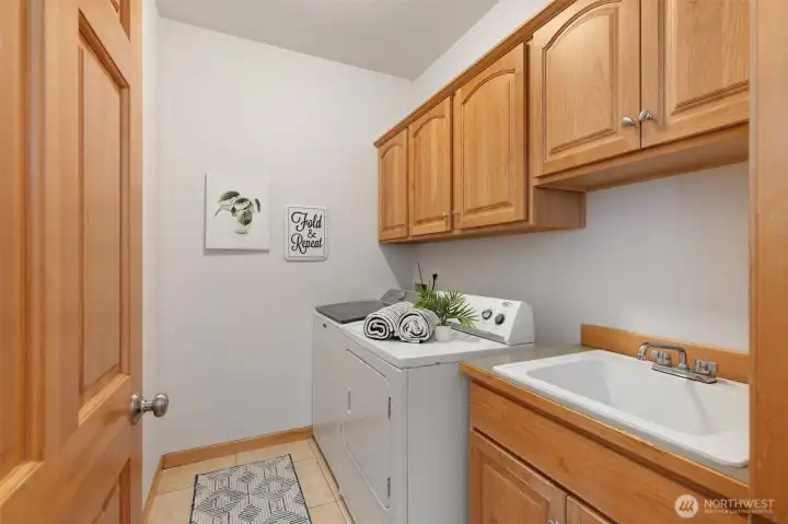 Spacious laundry room with ample cabinets/storage and a utility sink.