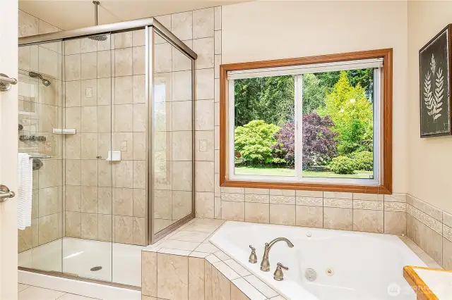 Unwind in the large jetted tub beneath a window that frames a peaceful view of the trees—no privacy glass needed. The tiled walk-in shower features both a rain shower and standard shower head for a spa-like experience.