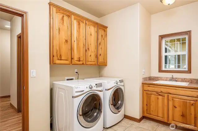 Spacious utility room with full-sized front-loading washer & dryer, a convenient utility sink, and beautiful wood cabinetry to keep laundry supplies neatly tucked away.”