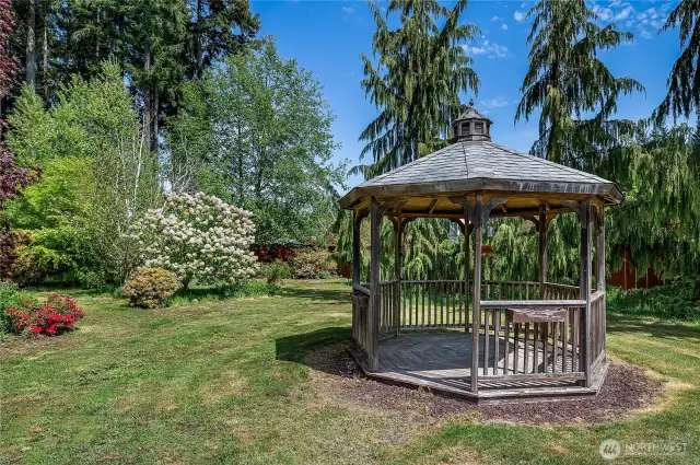 Charming gazebo nestled in the backyard offers a serene retreat with views of lush trees, vibrant rhododendrons, and fragrant lilacs. A peaceful spot where birds love to visit.