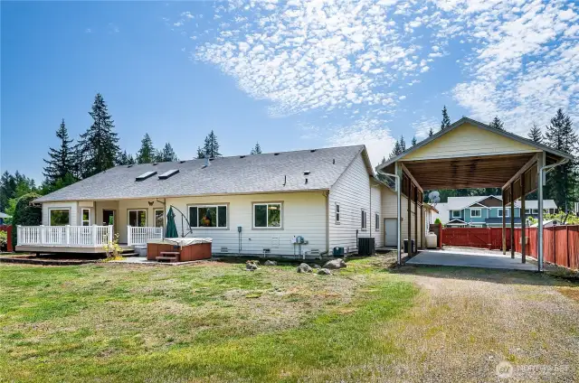 Rear view of the home featuring spacious covered RV parking. The propane tank in the distance is owned (not leased) and conveys with the property!
