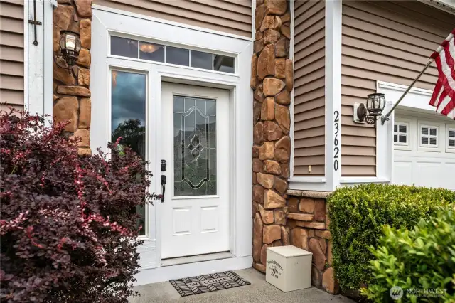 The home welcomes you with a leaded glass front door, classic sconce lighting, and elegant stone accents.