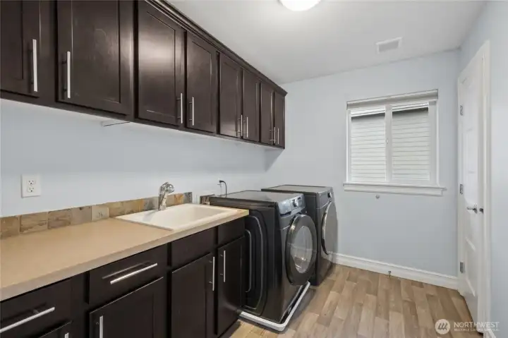 Thoughtfully located upper-floor laundry room offering abundant cabinetry and front-load washer and dryer.