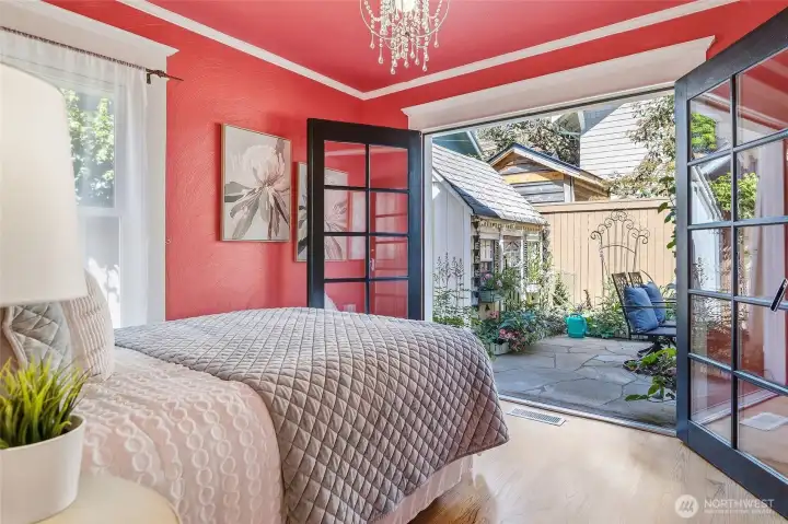 Bedroom 1 with french doors open to lush backyard with cute shed, gazebo and fire table (all stay)
