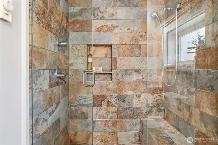 Remodeled primary bathroom large shower with bench and shampoo niche.