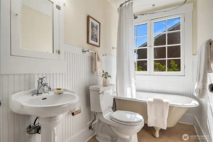 The second floor bathroom is also a full bath with painted wainscoting and a cast iron tub on marmoleum floors.