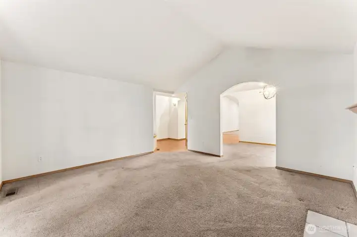 Looking across the living room toward the entry, the layout clicks into place. The arched doorway leads straight into the dining room and back around toward the kitchen, creating a circular floor plan that keeps you from hitting dead ends as you move through the house. The vaulted ceiling peak adds a nice architectural touch, and the recently installed gas furnace keeps the temperature steady with efficient forced air heat throughout the home.