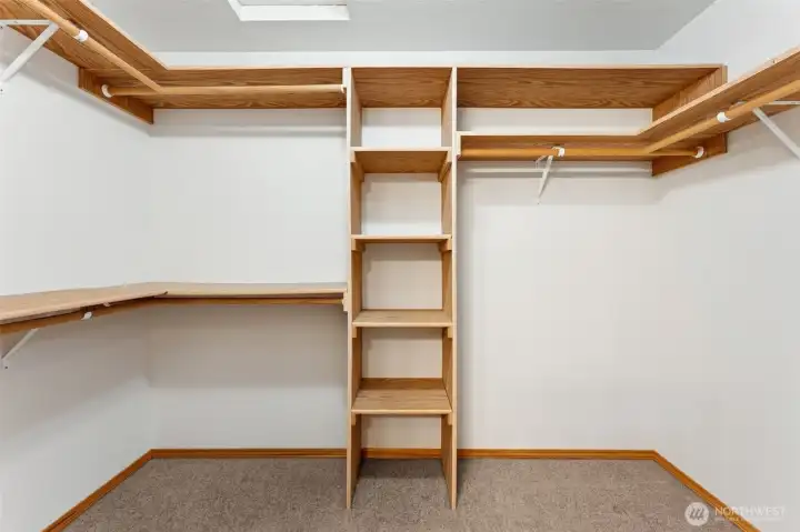 A proper walk in closet with a little separation, thanks to the pocket door that closes it off from the bathroom. Built in shelving lines the space, wood storage above takes care of extras, and attic access lives right overhead for the long term storage bins. The carpet underfoot makes the morning routine more comfortable, especially right after a hot shower when cold floors are the last thing you want.