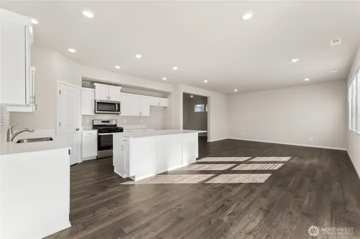 Open-concept kitchen and great room featuring shaker style cabinets, stainless steel appliances including gas range and over-the-range microwave, large island, luxury laminate plank flooring, and abundant natural light from windows. Photos are representative only and may display different color package and/or upgrades.