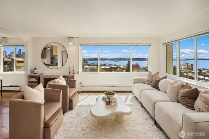 The living room — bright, airy, and framed by incredible views of Elliott Bay and the Olympic Mountains. Hardwood floors, baseboard heat, and wall-to-wall windows fill the space with natural light. The monthly assessment of $844 includes property taxes, water, sewer, garbage, and common area maintenance.