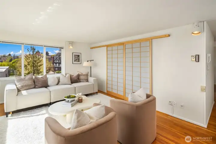 Living room at its best — Elliott Bay, ferry traffic, and the Olympic Mountains as your daily backdrop from the 6th floor. The flexible layout easily accommodates multiple seating areas. The shoji screen wall to the right separates the 2nd bedroom from the living space — open it up and the whole unit opens up with it.