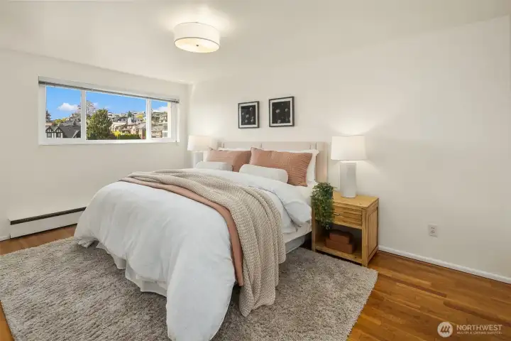 Primary bedroom that can fit a king size bed— spacious and serene, with hardwood floors, baseboard heat, a large closet, and a window overlooking the quiet residential neighborhood of Queen Anne. Freshly painted interior and new light fixture. Peaceful and private on the top floor.