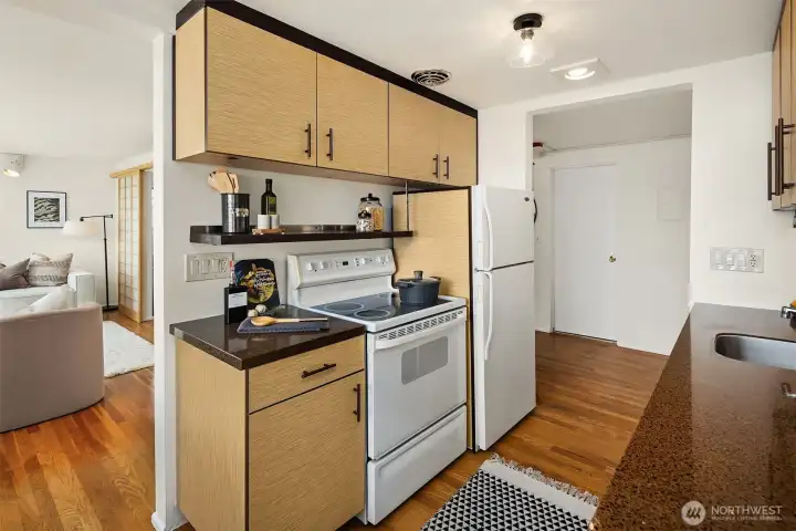 Another angle of the kitchen showing the range, refrigerator, and open sight line into the living room — the floor plan lives large and connects the spaces beautifully.