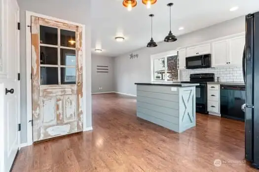 View looking toward living area and kitchen from dining room. White washed antique window pane door to panty compliments the wainscoting in dining area and custom designed island.