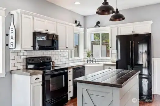 This kitchen offers cement counter tops, white subway tiles and cabinetry, farm style sink with new faucets, corner window, new lighting and highlights the dark wood counter top on island.