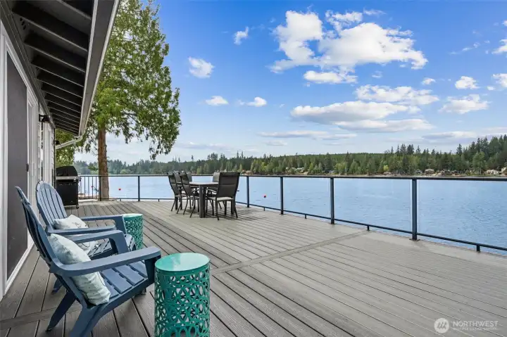 Brand new and stretching across an astonishing 2,000 square feet, it creates a true outdoor living experience instead of just “a place for two chairs and a sad grill.” The glass railing panels keep the sweeping Mason Lake views completely open, letting the water and sunsets take center stage from nearly every angle. There is room here for outdoor dining, lounge seating, grilling stations, cocktail hours, yoga at sunrise, chaotic family barbecues, honestly all of it, and because the home faces west, the afternoon and evening light absolutely pours across the deck in that golden-glow way people spend fortunes trying to recreate elsewhere.