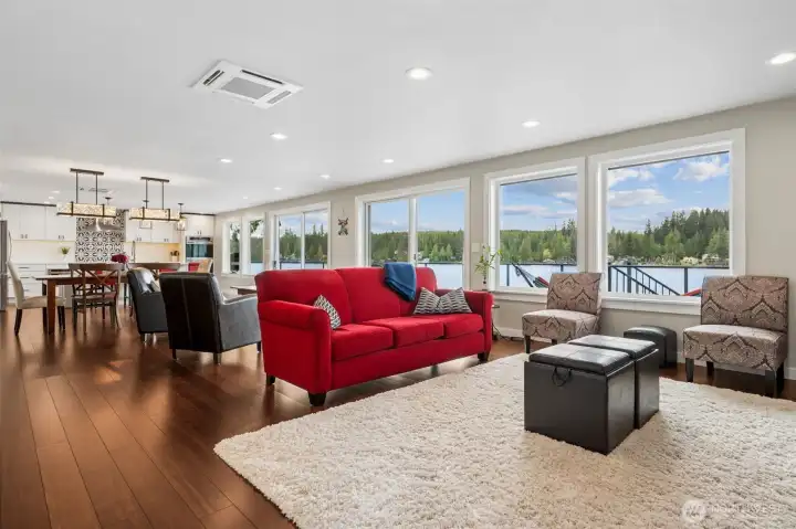 The entire back wall of the home opens to Mason Lake through dramatic near floor-to-ceiling windows, pulling the water, sky and sunset views straight into the living space like living artwork. Those wide plank coffee-toned hardwood floors stretch through the entire open-concept layout, connecting the living room, second sitting area, dining space and kitchen into one long, effortless flow built for entertaining, weekend guests or simply living really well every day.