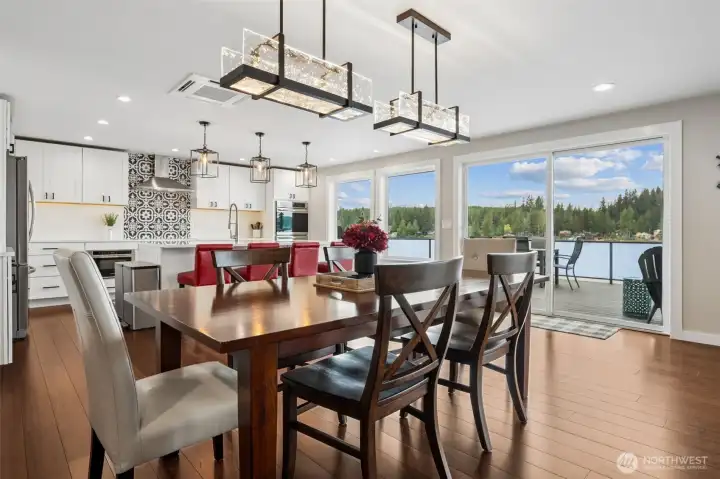 Those two contemporary chandeliers bring just the right amount of drama overhead, anchoring the space beautifully while still letting the lake remain the main event beyond the windows. Room for a substantial table here, while the connection to the kitchen works perfectly too. Guests gathered around the island can still be part of the conversation, while the dining area maintains enough separation to feel intentional.