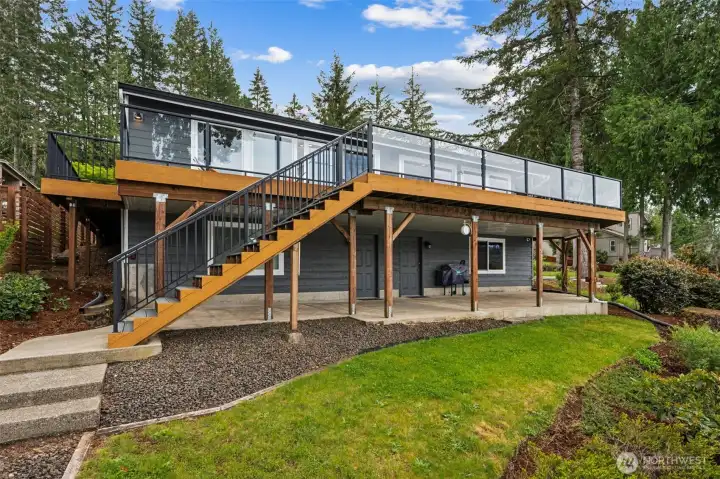 The back of this home is serving full modern lake-house energy. That brand new 2,000-square-foot composite Trex deck completely transforms the rear elevation into a showpiece, with sleek metal and glass railings keeping the views wide open while adding a clean contemporary edge to the home’s remodel. And that staircase floating gracefully down toward the waterfront? Gorgeous. Below, the covered concrete patio connects directly to the two lower-level flex rooms, each with its own exterior entrance and window, creating all kinds of intriguing possibilities for future guest suites, hobby rooms, creative studios or private hangout spaces. The landscaping keeps things polished without becoming high-maintenance, with gravel accents, lawn areas and tidy planting beds all leading naturally down toward the waterfront path.