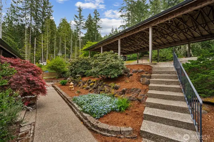 This landscaping has that established lake-house charm that makes a property feel loved the second you arrive. Set on a .34-acre lot, the home is surrounded by thoughtfully layered planting beds, mature greenery and broad welcoming steps leading up toward the impressive four-car carport, and let’s be honest, at a lake house, extra parking matters more than people think. Between guests, lake toys, extra vehicles and summer weekends that somehow turn into mini reunions, having flexible parking options under the carport, along the driveway and near the tree line is genuinely valuable. The shared driveway arrangement with the neighboring homes keeps the setting feeling tucked away and connected rather than isolated, and it certainly does not hurt that the neighbors here are known for being friendly!