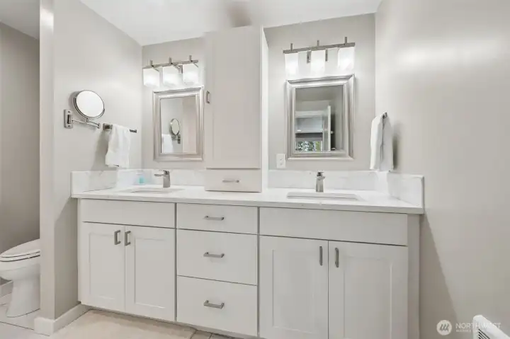 This en suite keeps layering in thoughtful details. The privacy wall for the toilet creates a more elevated layout instead of everything being awkwardly on display the second you walk in, and beyond it sits a generous dual-sink vanity with undermount sinks and excellent storage. The tall cabinet dividing the vanity areas is such a smart addition too, adding function while subtly giving each side its own space. Warm neutral tile floors keep the bathroom feeling soft and timeless, and then we get to the underrated luxury feature everyone secretly loves, the separate wall heater. Because being able to crank the bathroom warmth after a shower without turning the entire house into a sauna is genuinely fabulous.