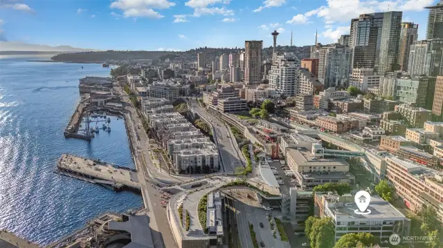 Experience breathtaking aerial views from this Seattle waterfront condo, showcasing the sparkling Puget Sound, bustling marinas, and the iconic Space Needle piercing the skyline. The photo highlights the prime location near the new 20-acre Waterfront Park, with downtown's vibrant energy and distant mountain vistas in full display. The building's strategic spot, marked by the home pin, promises unmatched proximity to water and city life, making every glance out your window a postcard-worthy moment!