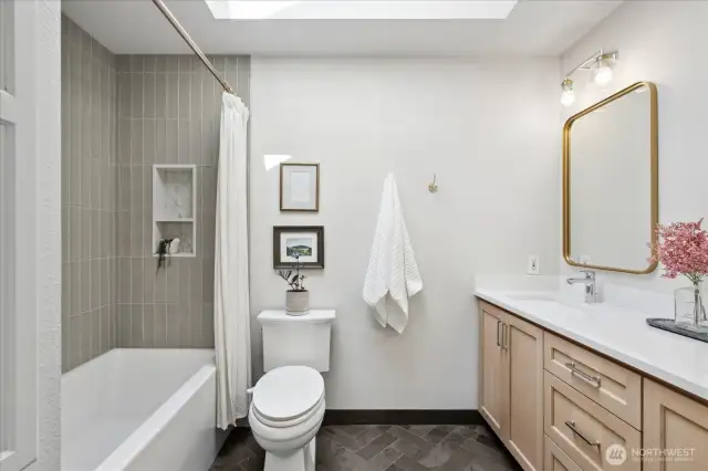 Primary bathroom with heated herringbone, black slate floors. Skylight provides great lighting