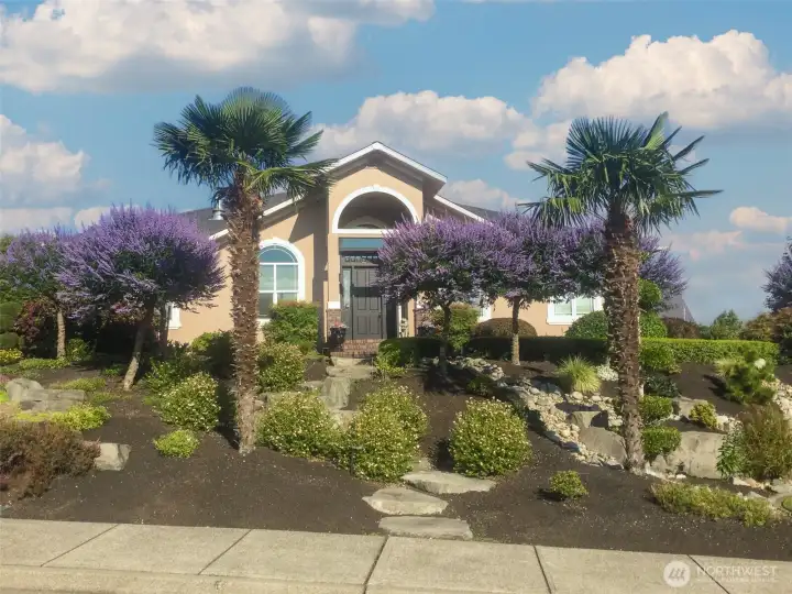 Stone step pathway winds through vibrant landscaping and sculpted greenery, creating a striking welcome to the front door.