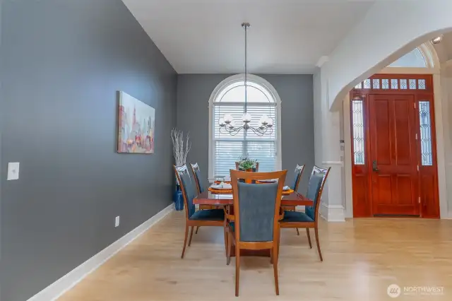 Elegant dining room with soaring ceilings, rich accent wall, and a grand arched window that fills the space with natural light—perfect for gatherings.