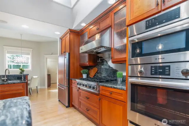 Chef’s kitchen featuring Bosch double ovens, a professional-grade Viking gas cooktop with striking granite backsplash, and cherry cabinetry that blends beauty with function.