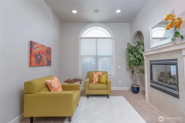 Cozy sitting area off the primary suite with soaring ceilings, arched window, and double-sided fireplace—perfect for quiet relaxation or a private retreat.