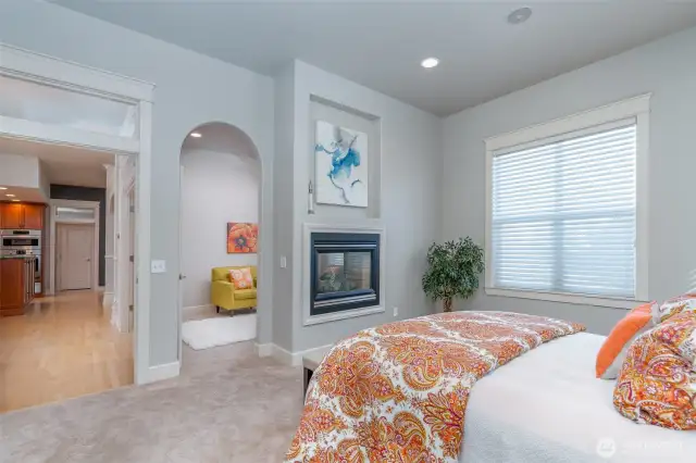 Another view of the expansive primary suite highlighting the double-sided fireplace and arched entry into the private sitting area—creating a warm and inviting retreat.