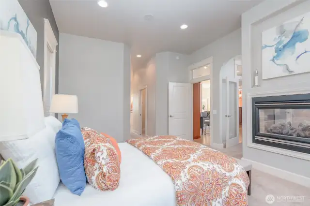 Expansive primary suite featuring elegant arches, transom windows, and an inset niche above the double-sided fireplace. Soft natural light and private entry to the spa-inspired ensuite bath create a true retreat.