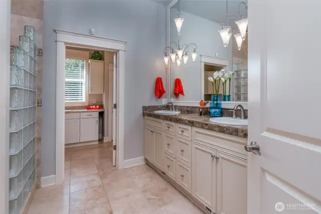Spa-inspired primary bath featuring radiant heated floors, dual sinks with marble-style counters, designer lighting, and a sleek glass-block shower wall—luxury and function combined.