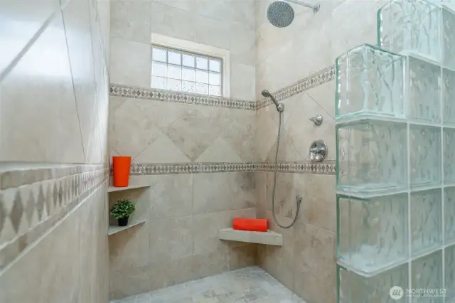 Luxurious walk-in shower with custom tile detail, glass-block accents, rainfall showerhead, handheld sprayer, and built-in bench seating—your own spa-like escape.
